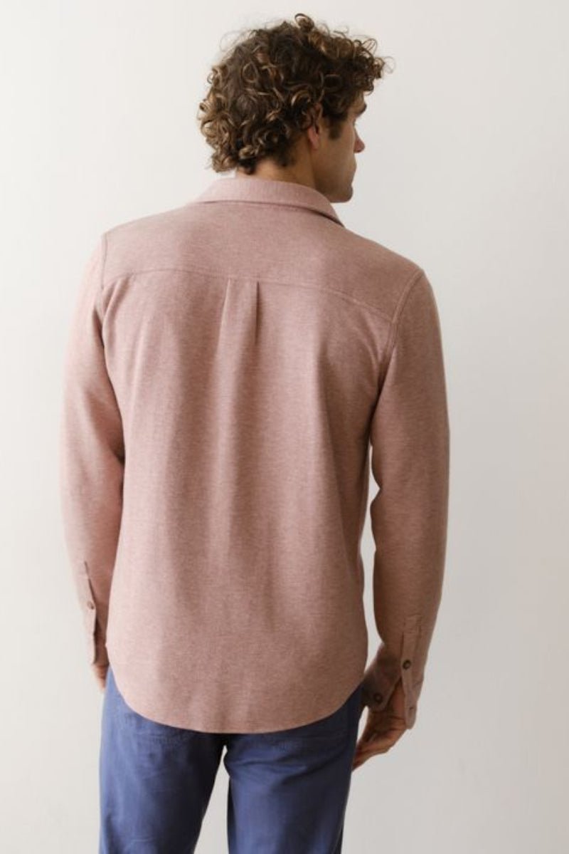 Man wearing a pink long-sleeve shirt and blue pants against a white background