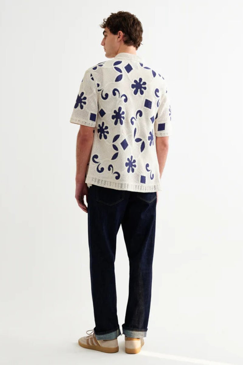 Person wearing a white shirt with blue floral patterns and dark pants on a white background