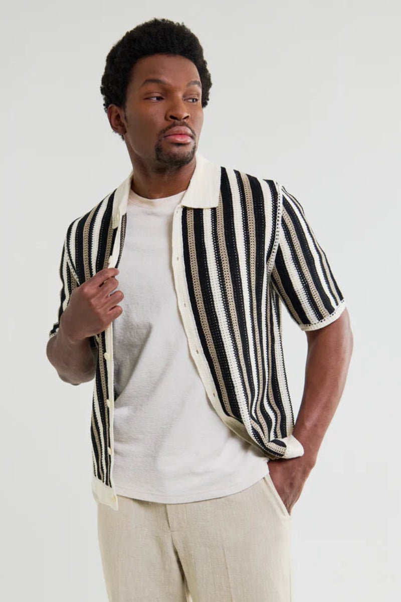 Man wearing a black and white striped shirt over a white t-shirt on a plain background