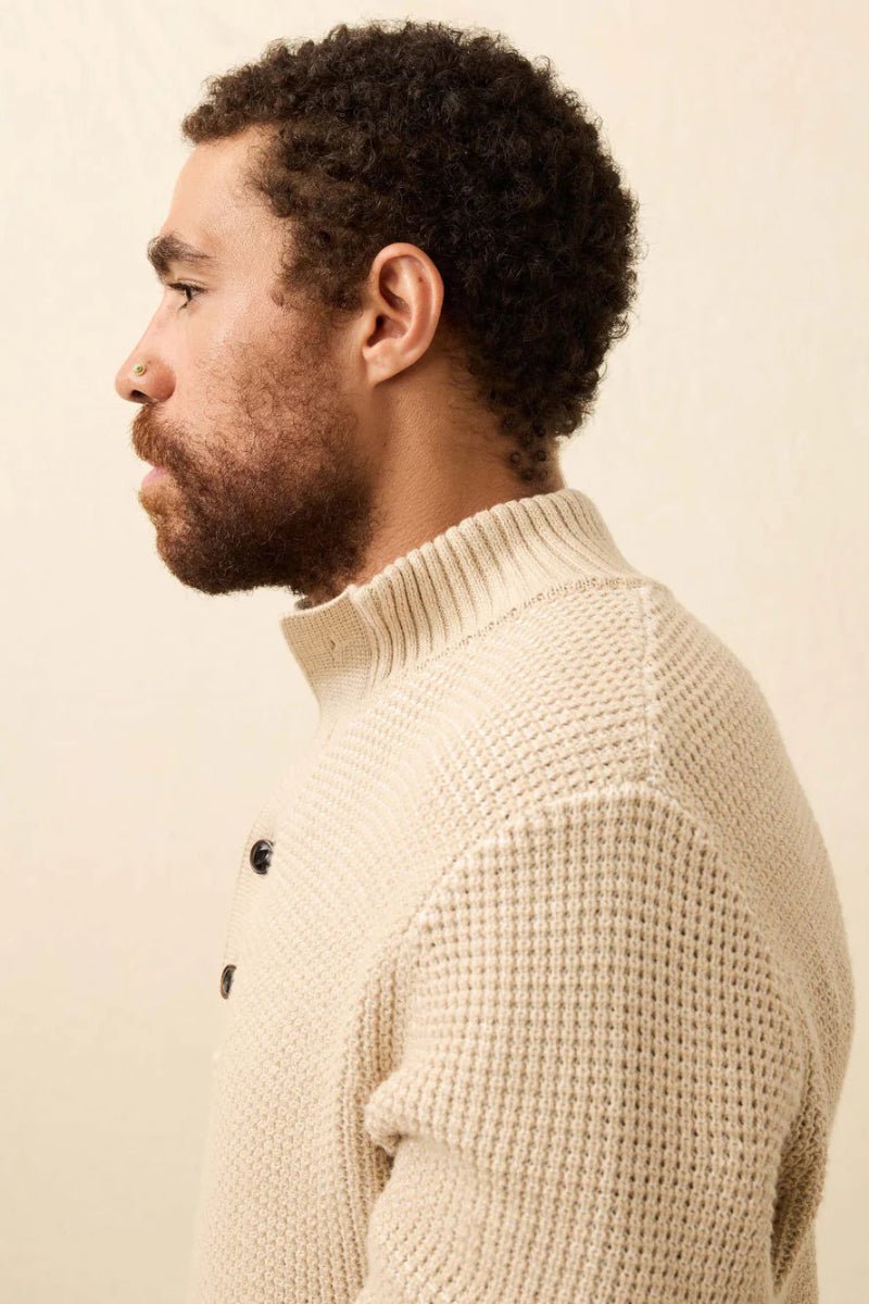 Man wearing a beige knitted sweater against a plain background