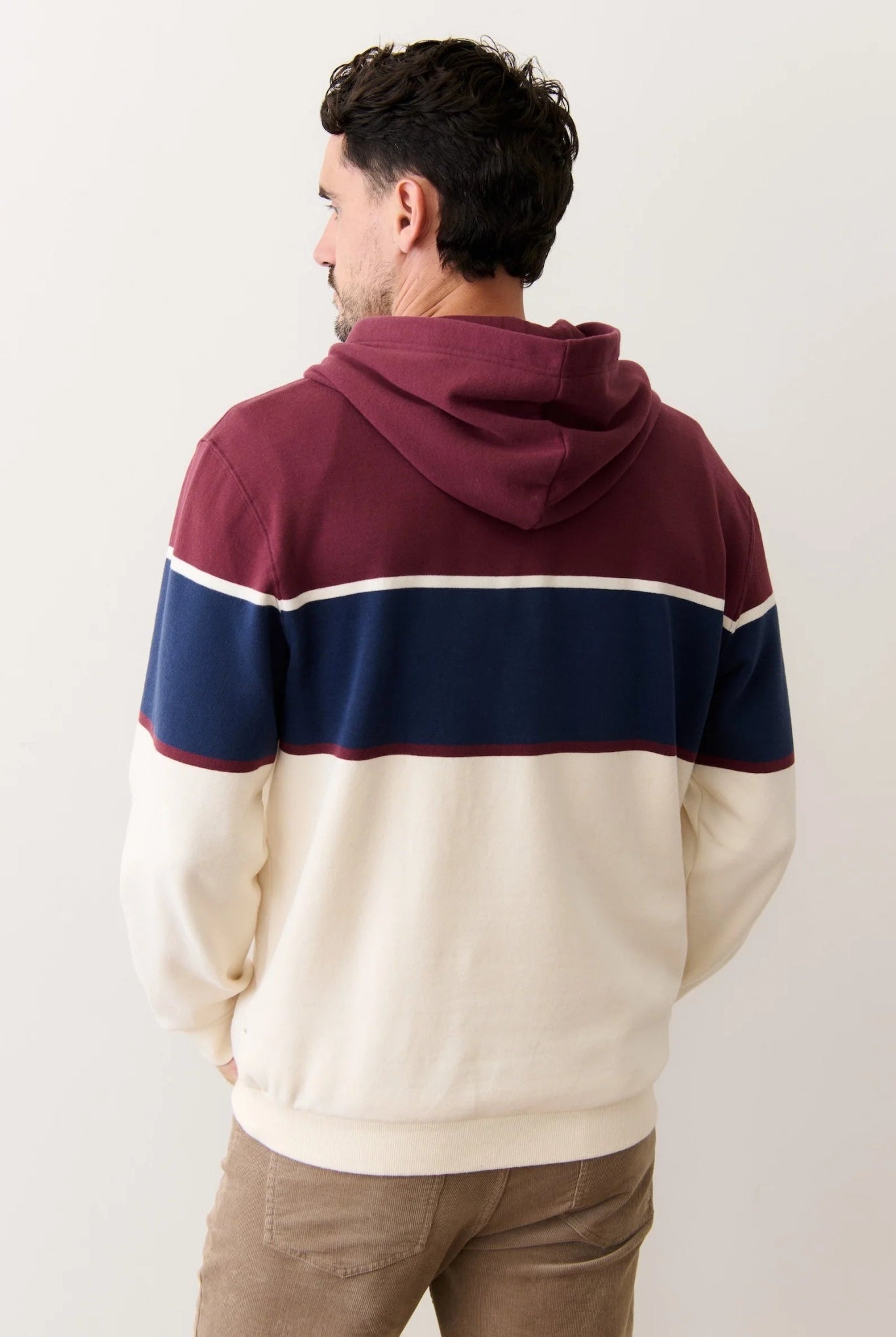Man wearing a color-blocked hoodie with maroon, navy, and beige sections on a plain background.