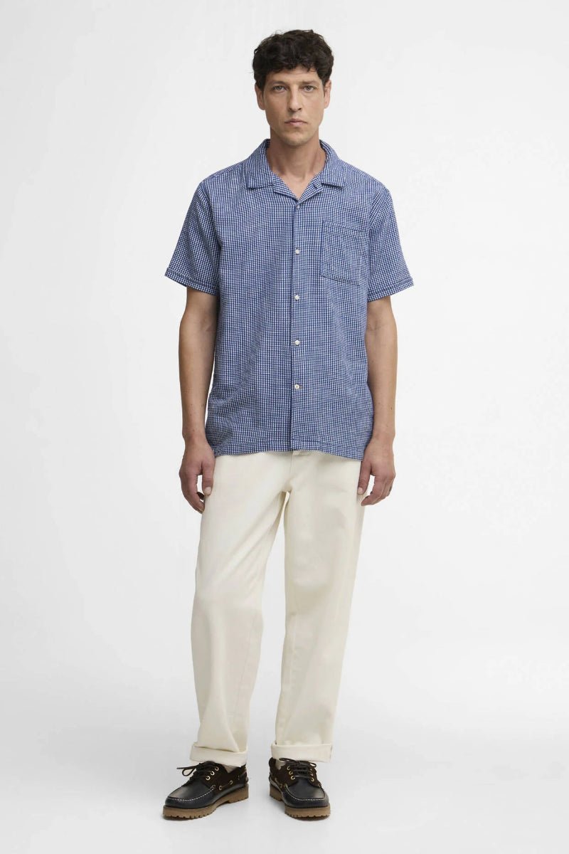 Man wearing a blue checkered shirt and beige pants on a white background