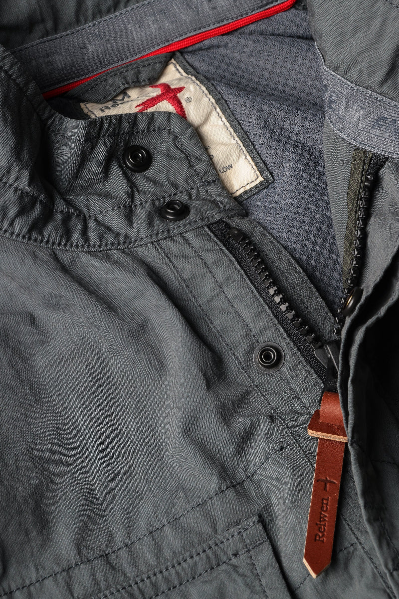 Close-up of a gray jacket with buttons and a leather strap, featuring a brand logo.