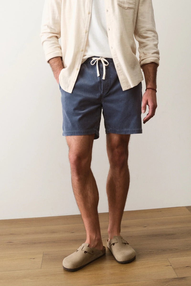 Person wearing blue shorts and a beige cardigan on a wooden floor.