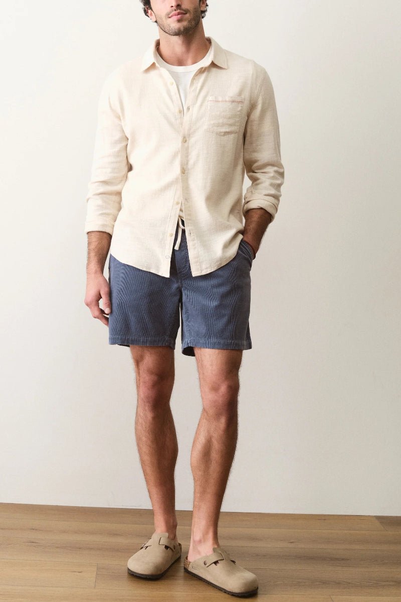 Man wearing a beige shirt and blue shorts against a plain background