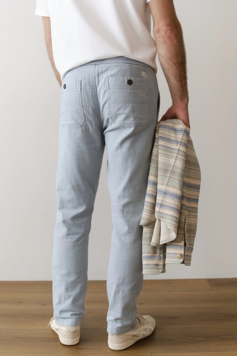 Person wearing light gray pants holding a striped shirt against a plain background