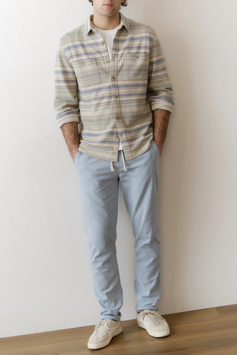 Person wearing a plaid shirt and light blue jeans against a white wall.