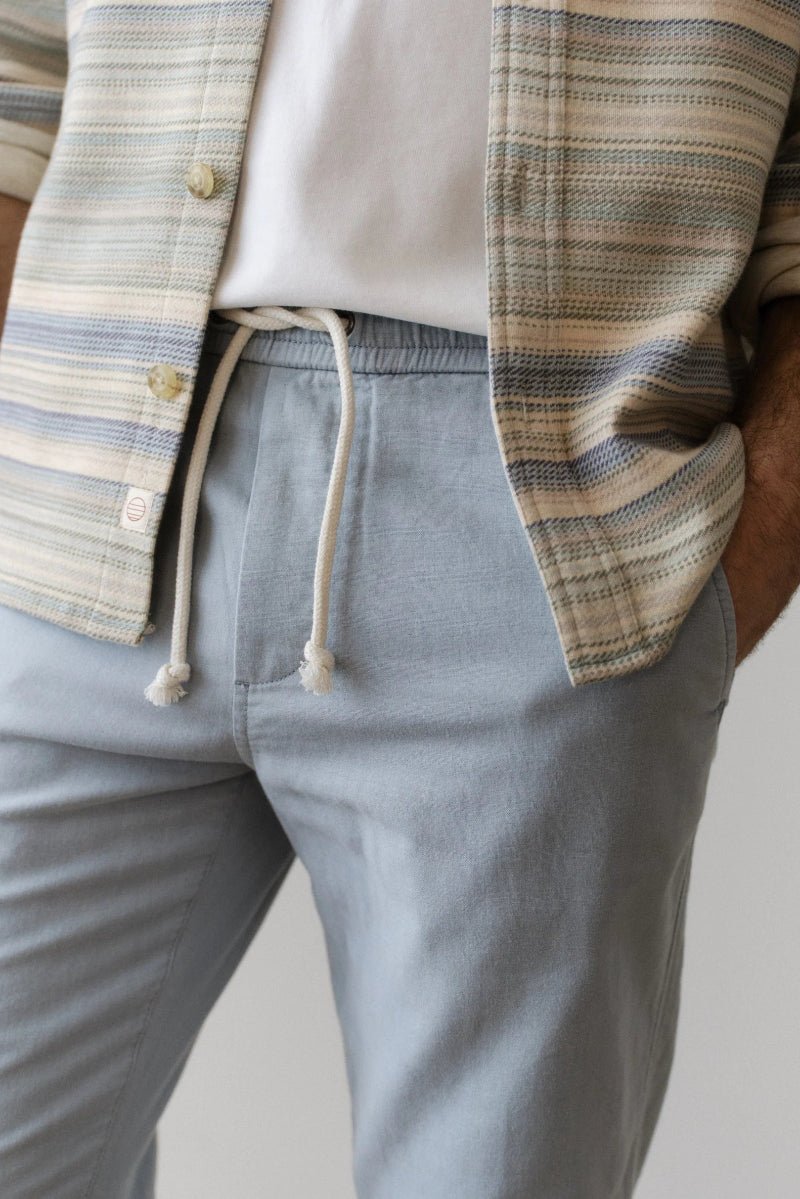 Person wearing a striped shirt and light gray pants with a neutral background