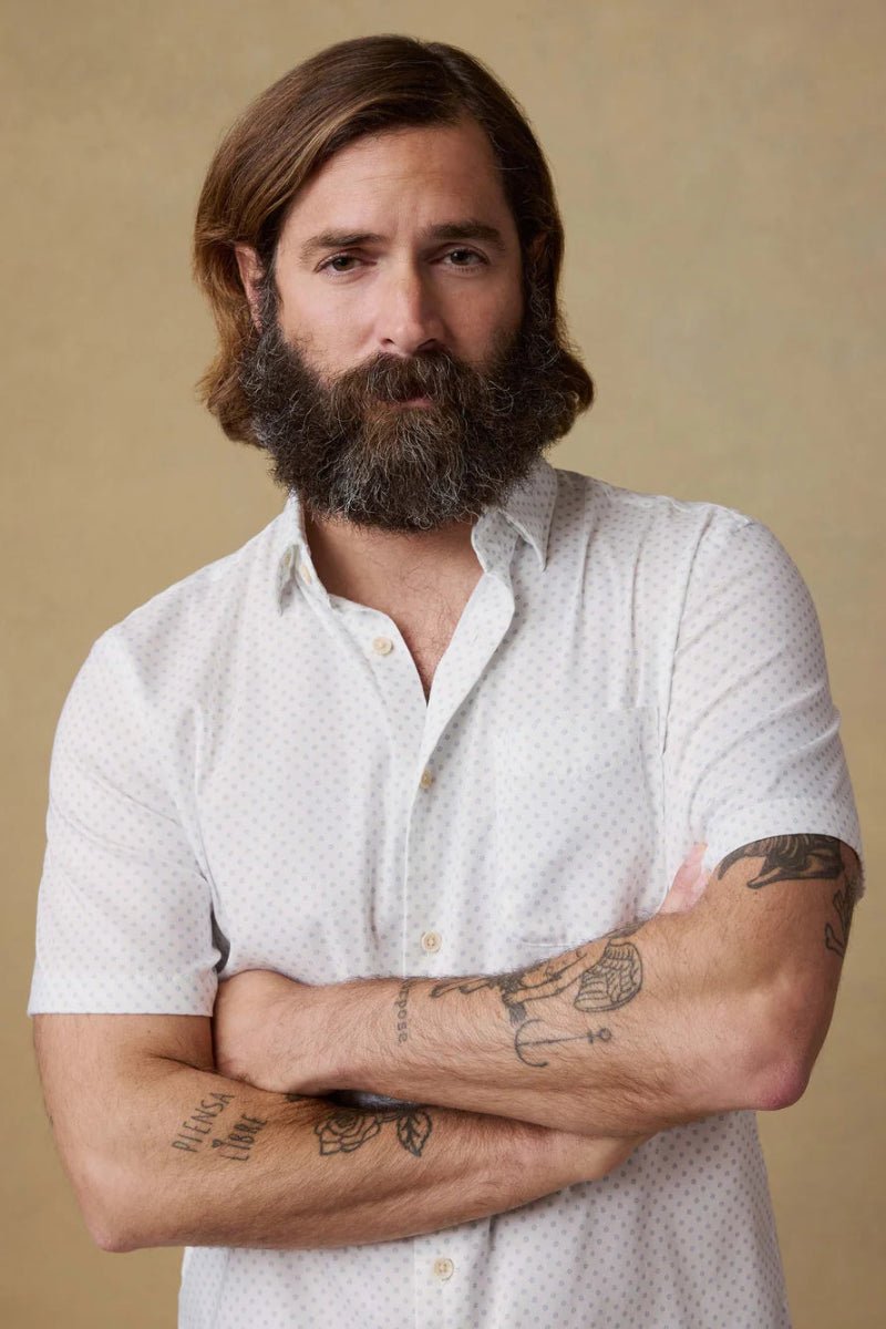 Man with a beard and tattoos wearing a white shirt against a beige background