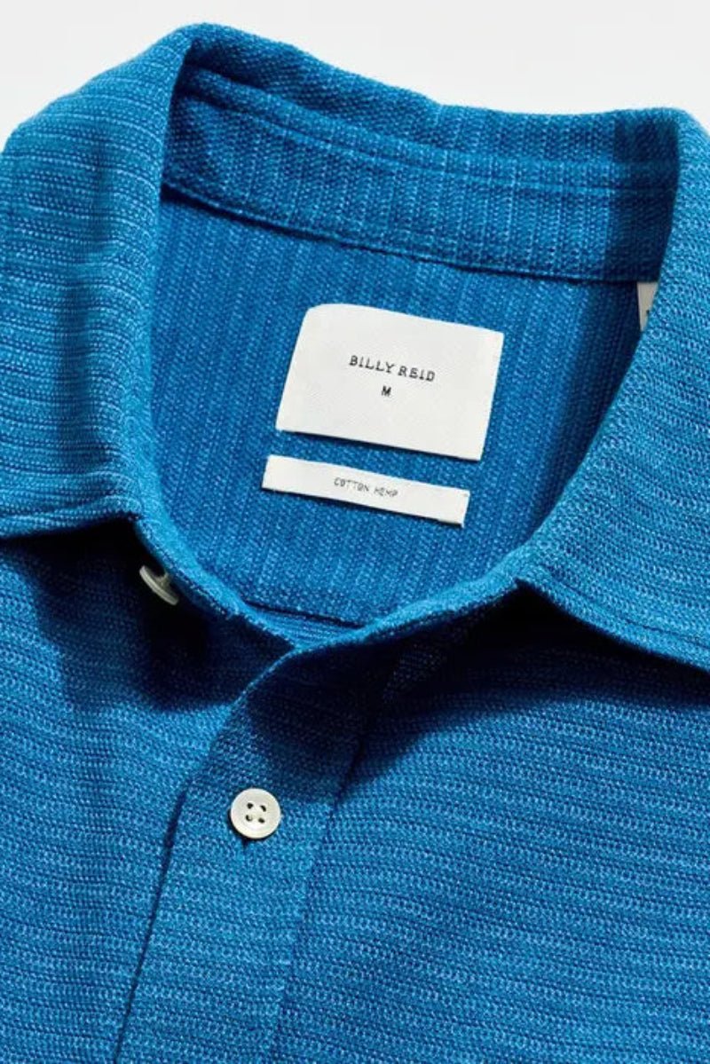 Close-up of a blue textured polo shirt with a brand label on a white background