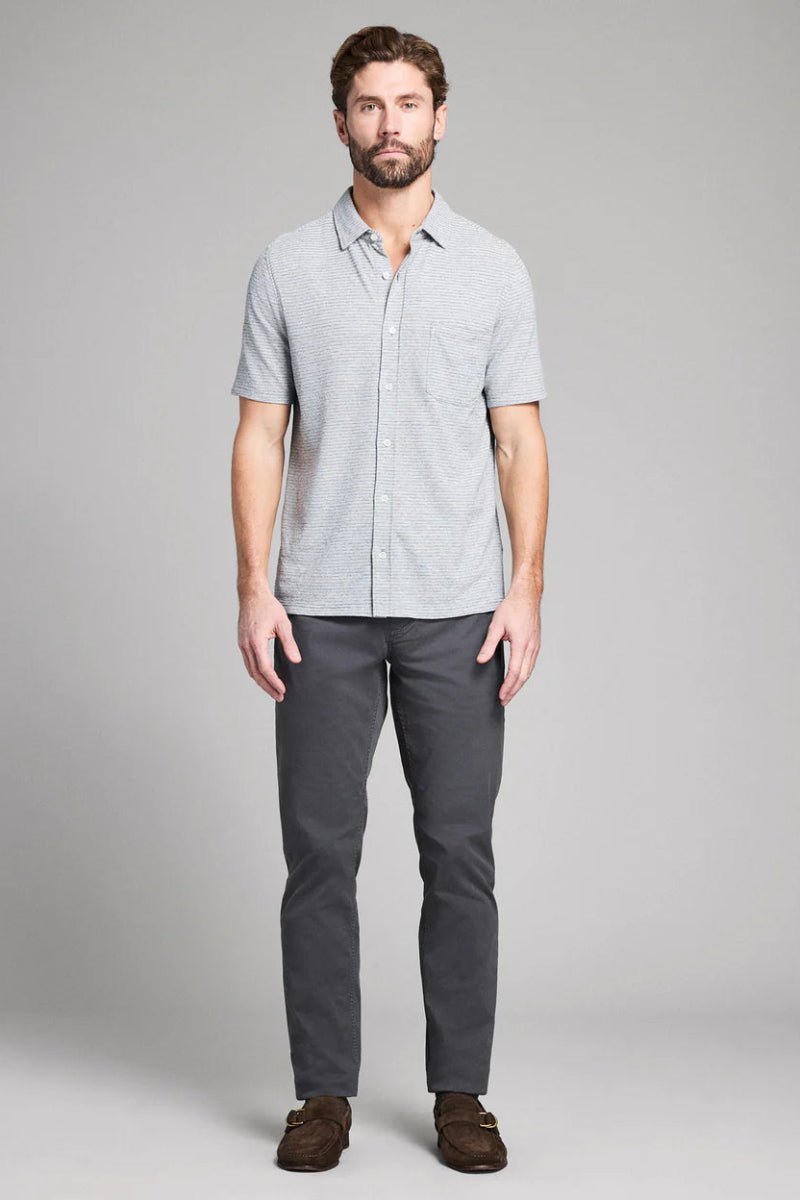 Man wearing a light gray short-sleeve shirt and dark gray pants on a plain background