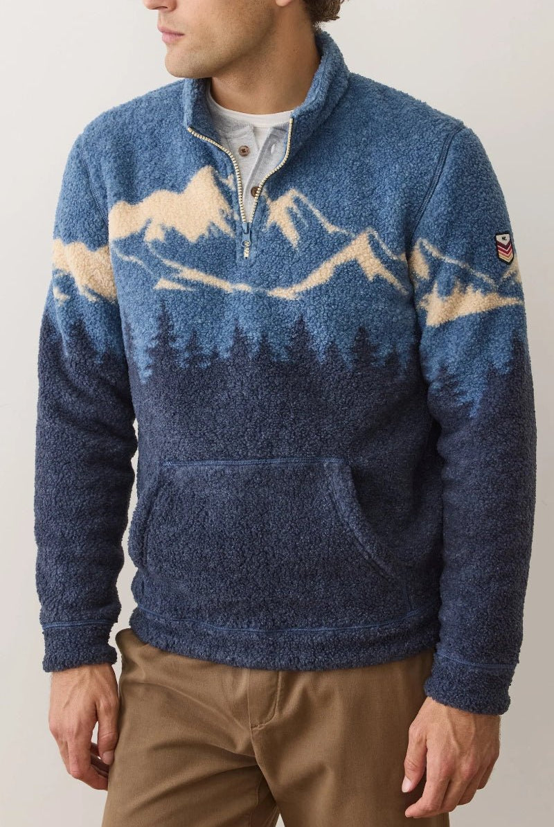 Man wearing a blue sweater with mountain and forest design against a plain background