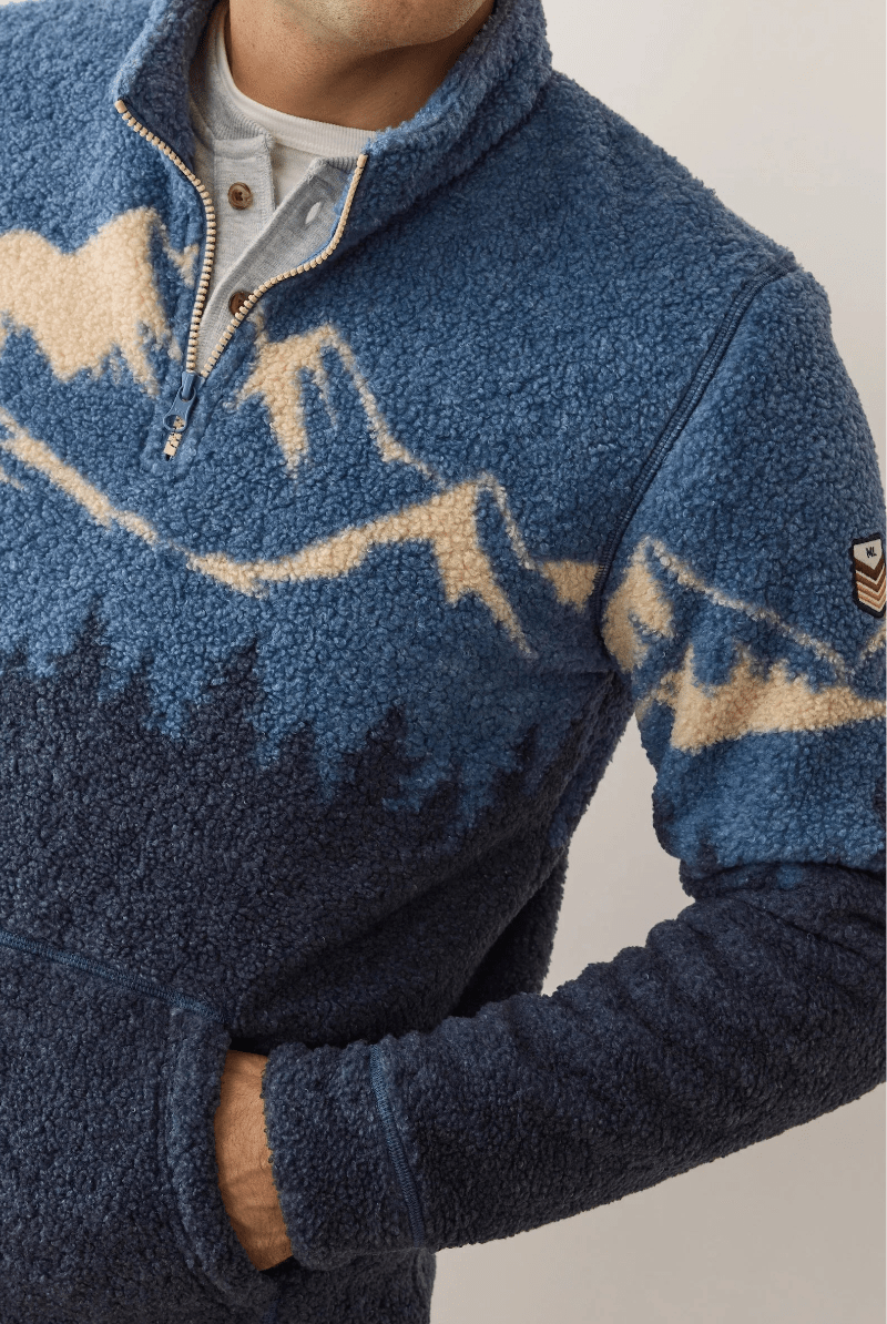 Blue fleece pullover with mountain design on a neutral background