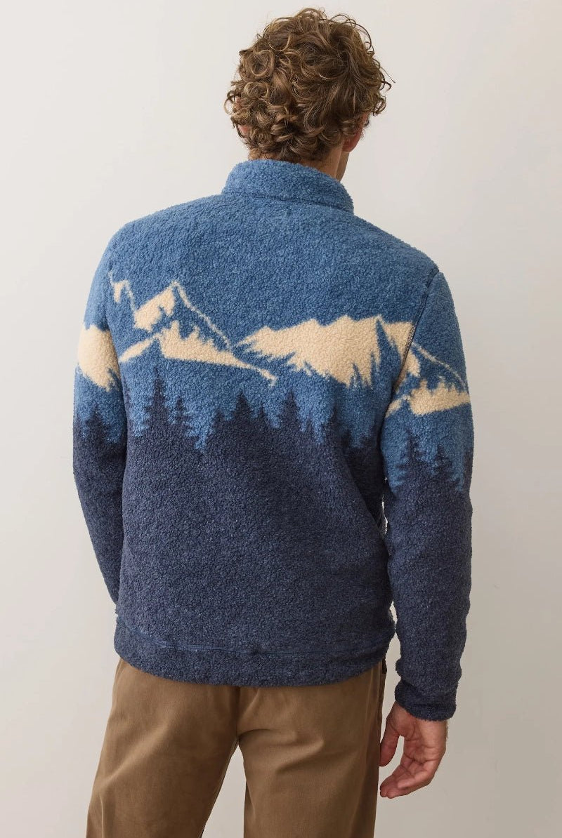 Person wearing a blue sweater with mountain design on the back against a plain background