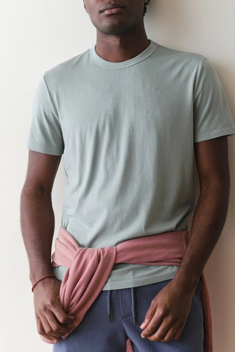 Person wearing a light gray t-shirt and pink fabric around the waist against a plain background