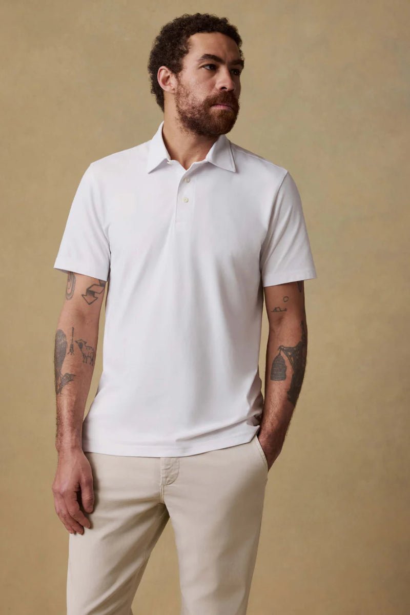 Man wearing a white polo shirt and beige pants against a beige background