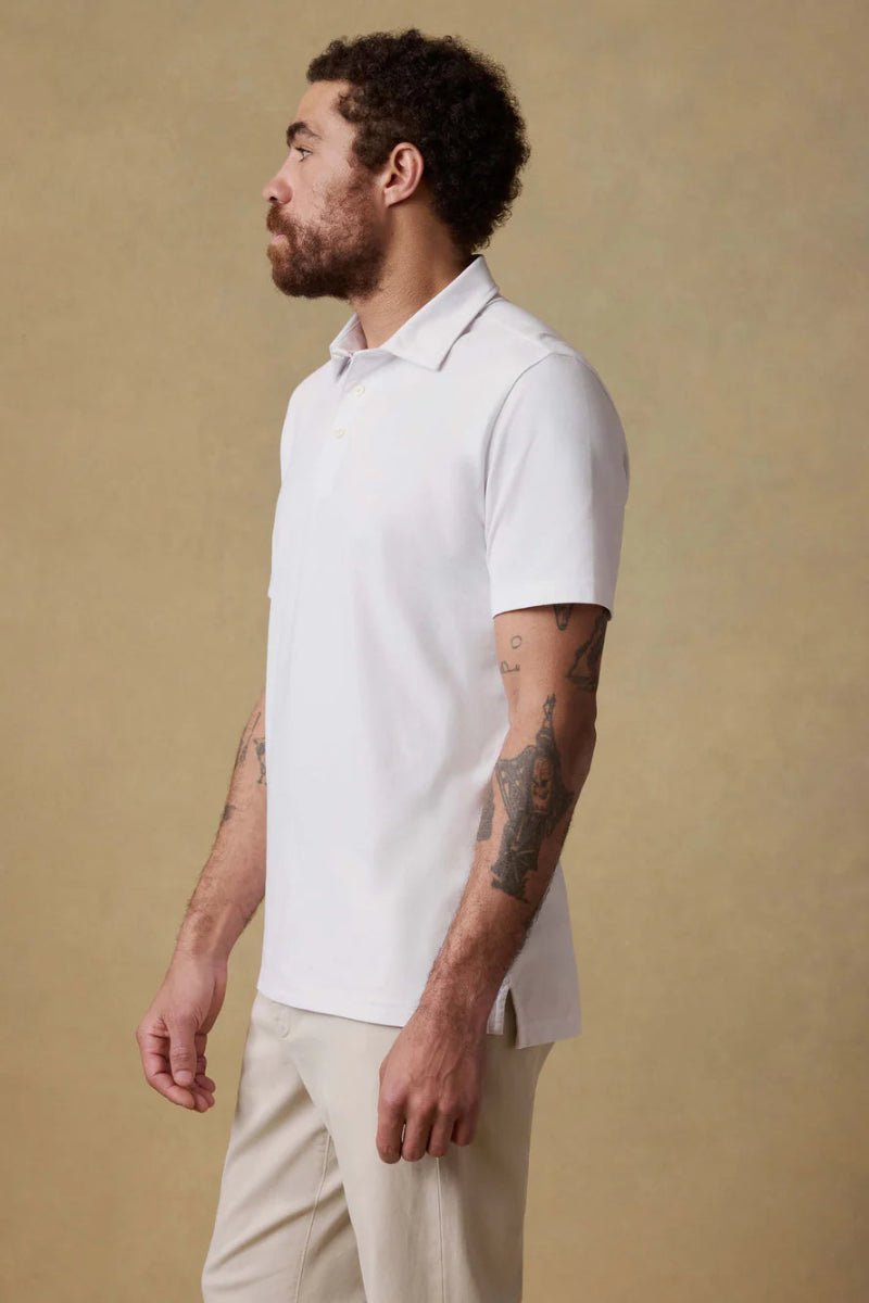 Man wearing a white polo shirt and beige pants against a beige background