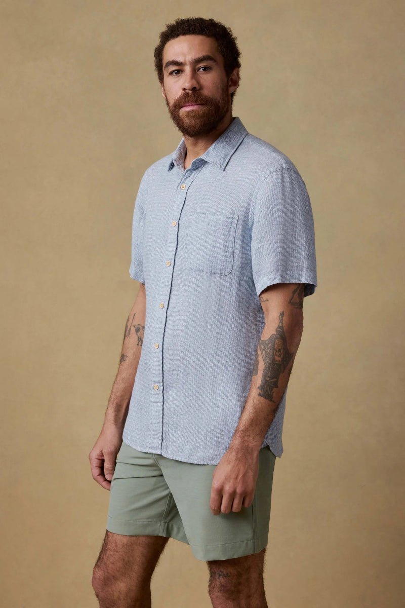 Man wearing a light blue shirt and green shorts against a beige background