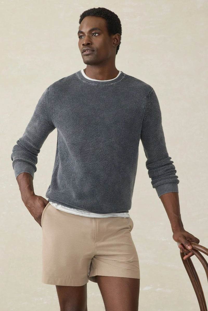 Man wearing a gray sweater and beige shorts against a neutral background
