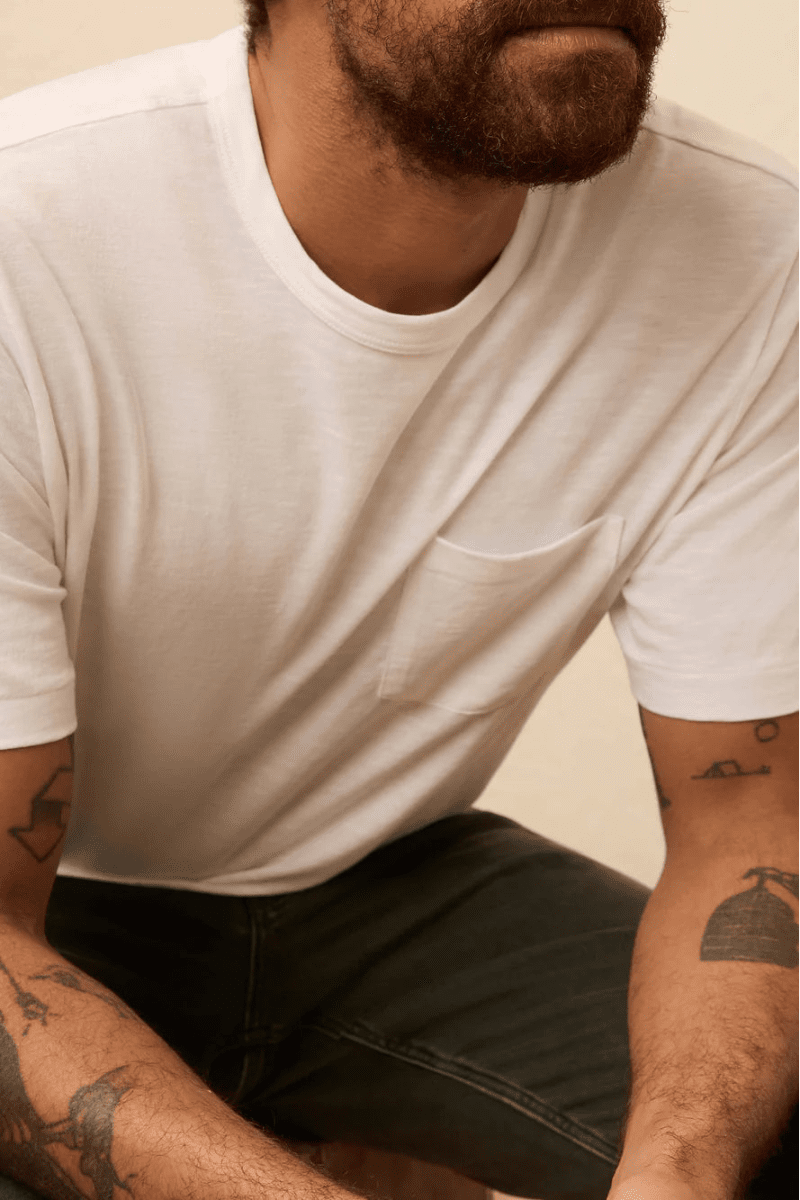 Man wearing a plain white t-shirt with tattoos on his arms.