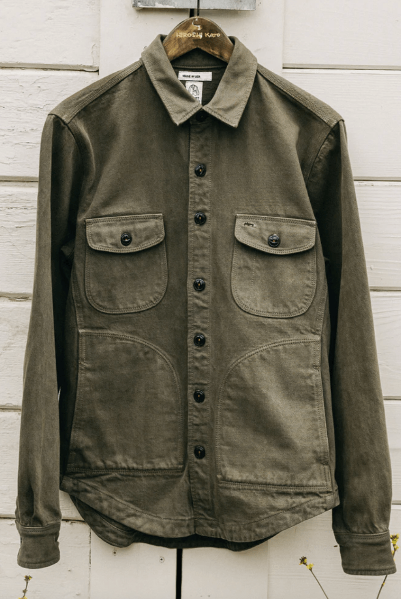 Green jacket with button details on a wooden hanger against a white wooden panel background