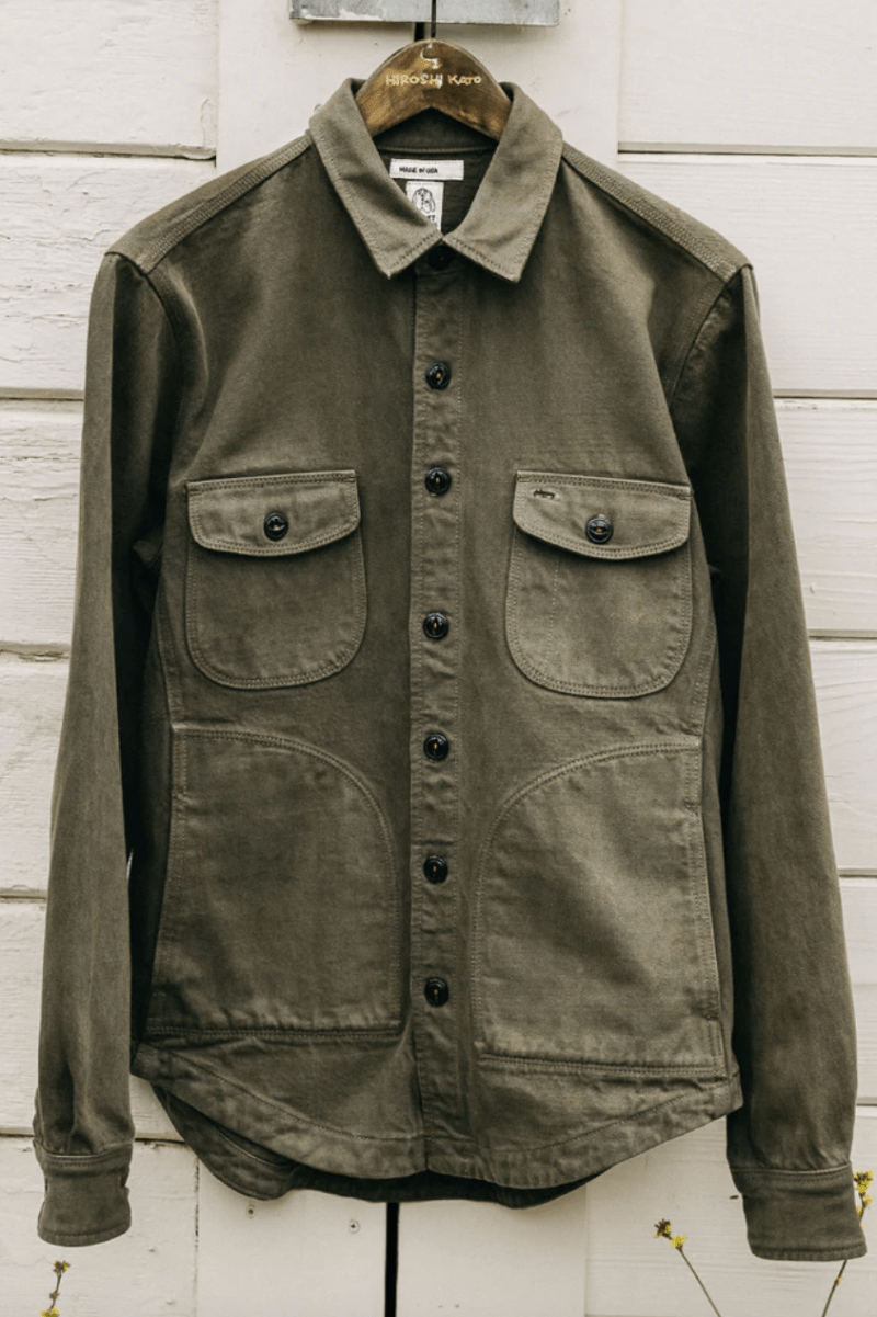 Green jacket with button details on a wooden hanger against a white wooden panel background