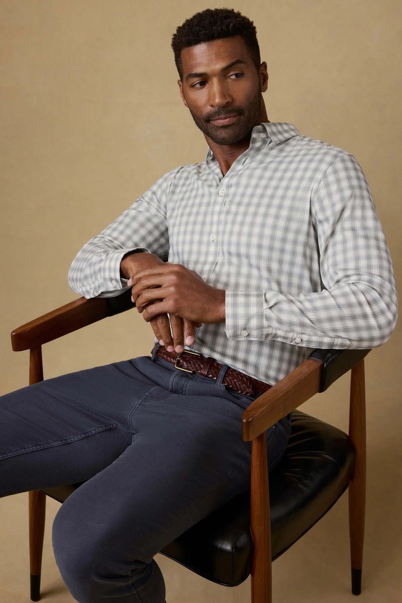 Man sitting in a chair wearing a checkered shirt and dark pants on a beige background