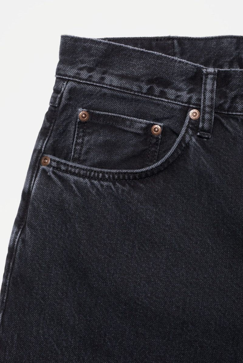 Close-up of black jeans with a brand logo on a light gray background