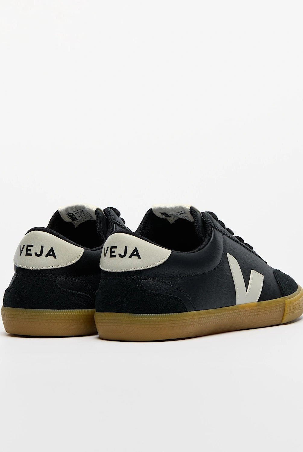 Black sneakers with white soles and 'Veja' branding on a light gray background