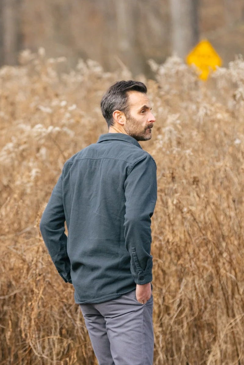 Man standing in a field of tall brown grass with a yellow sign in the background.