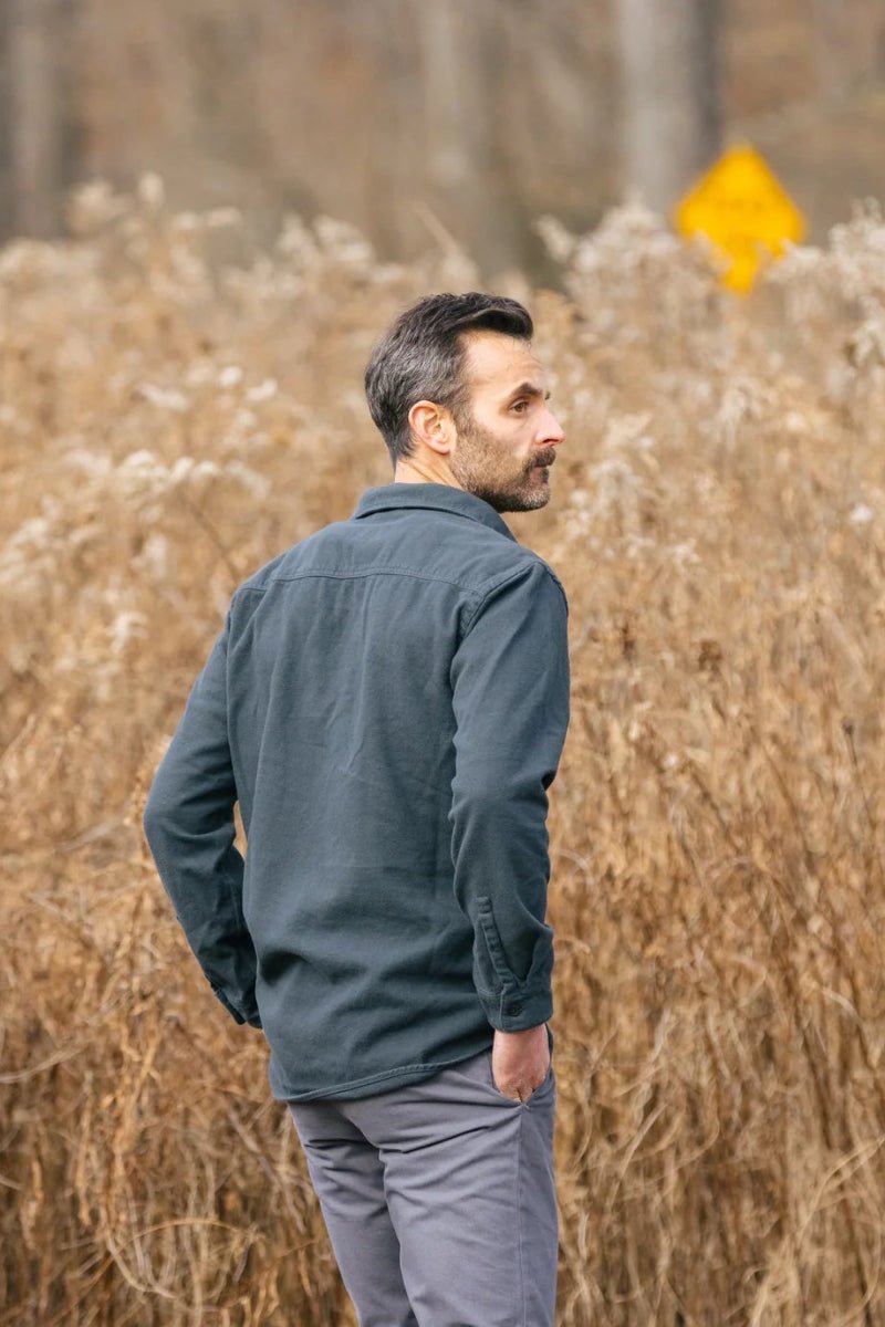 Man standing in a field of tall brown grass with a yellow sign in the background.