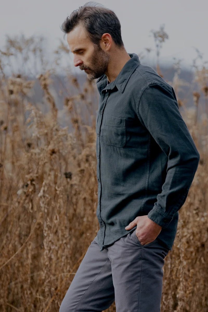 Man walking through a field of tall brown grass with mountains in the background
