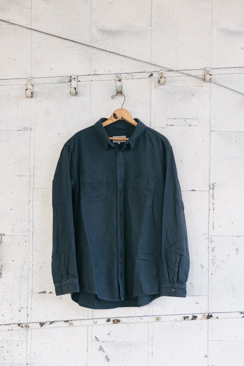 Dark green shirt hanging on a wooden hanger against a white textured wall.