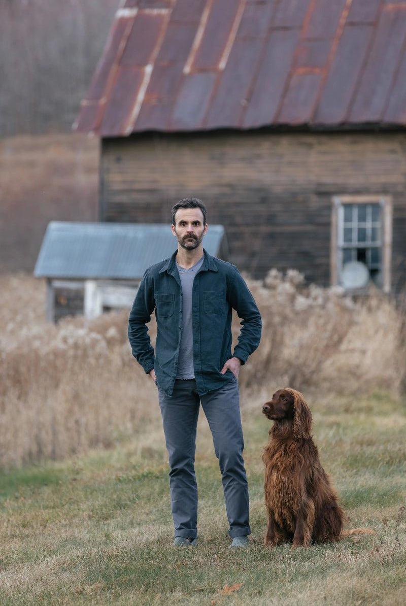 Man standing with a dog in front of an old wooden building