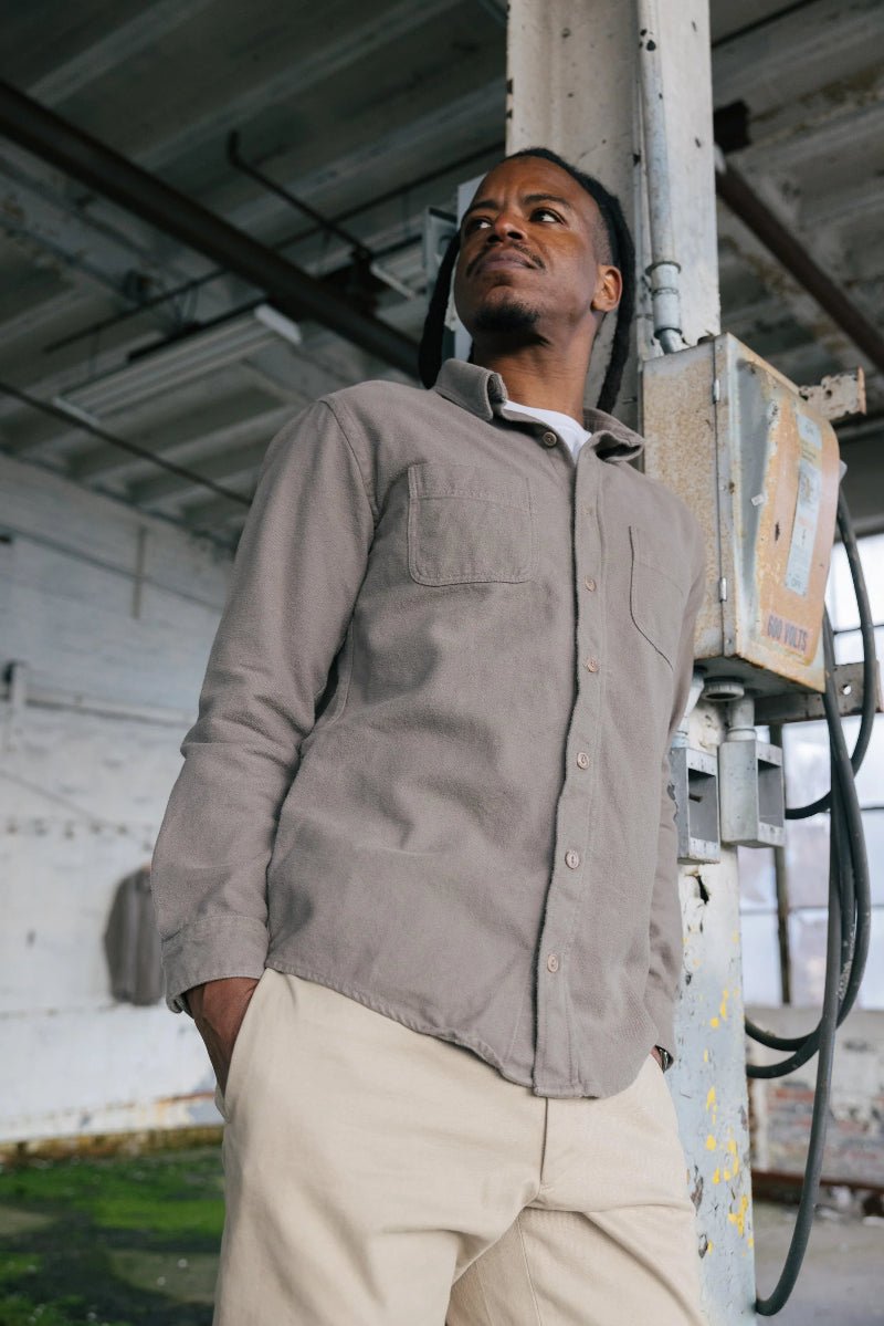Man wearing a brown shirt and beige pants standing in an industrial setting.