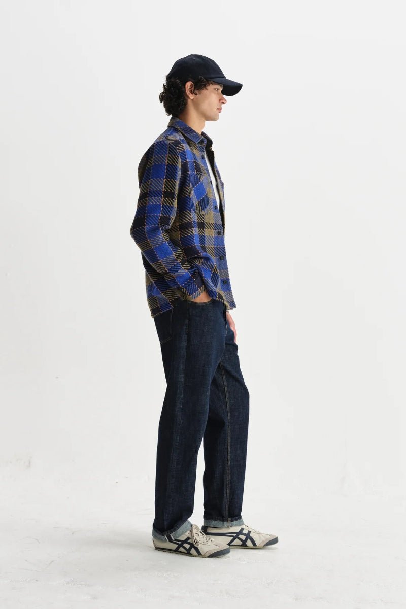 Person wearing a blue plaid shirt and dark pants on a white background