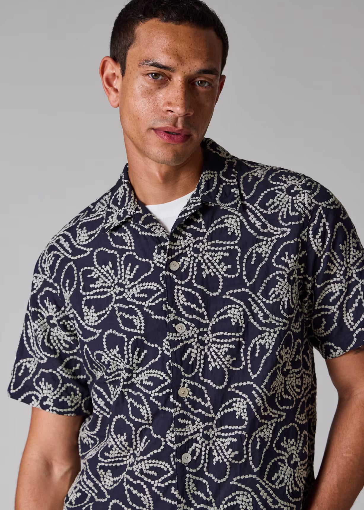 Man wearing a navy patterned shirt against a gray background