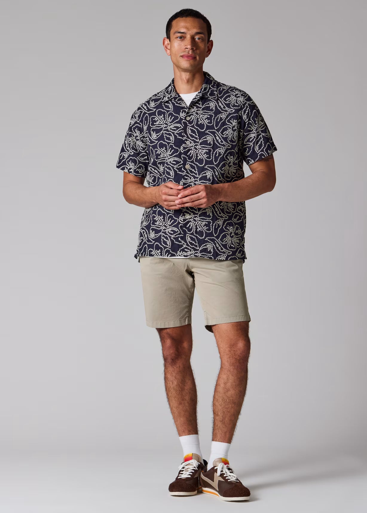 Man wearing a patterned shirt and beige shorts on a plain background