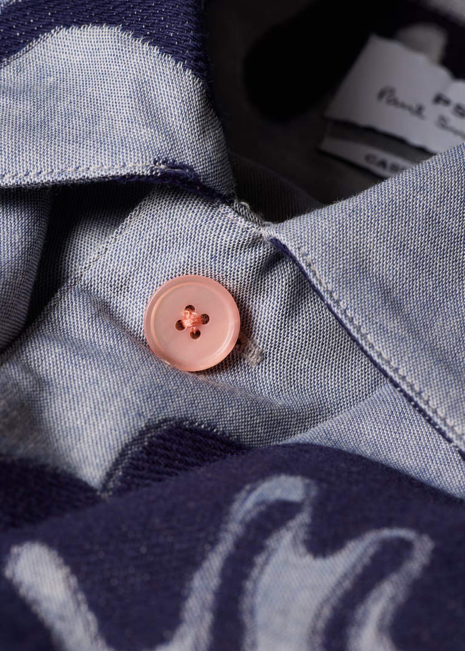 Close-up of a button on a denim shirt with a brand tag in the background.