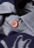 Close-up of a button on a denim shirt with a brand tag in the background.