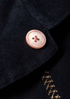 Close-up of a button on a dark fabric with gold embroidery.