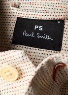Close-up of a 'PS Paul Smith' label on fabric with a button and other details.