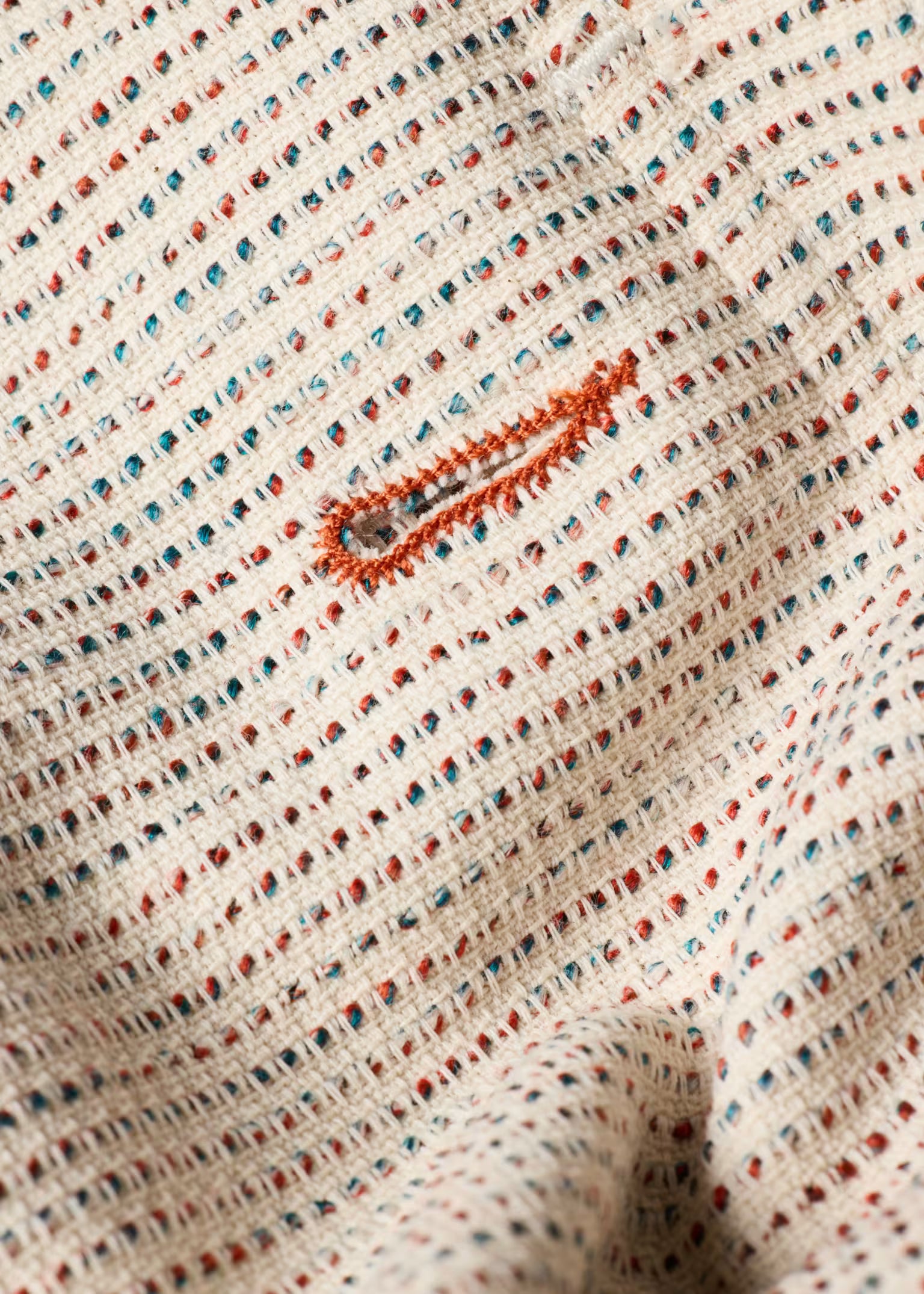 Close-up of textured fabric with a small embroidered design on a beige background