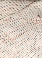 Close-up of a textured fabric with red and blue patterns on a beige background