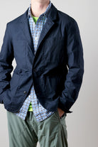 Person wearing a navy jacket over a checkered shirt with a plain background