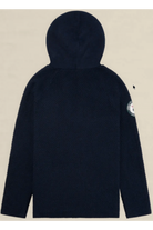 A dark navy blue textured hooded jacket shown from the back, featuring a circular patch on the left sleeve, set against a solid light beige background.