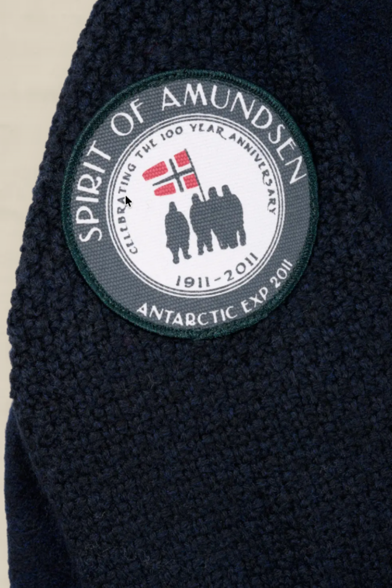 Close-up of a dark navy textured fleece garment with a circular embroidered patch on the shoulder. The patch reads 'SPIRIT OF AMUNDSEN' and 'ANTARCTIC EXPO 2018' with a flag and silhouettes in the center.