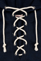 Close-up of a navy blue hooded sweatshirt with white laces threaded down the front and white drawstrings at the hood.