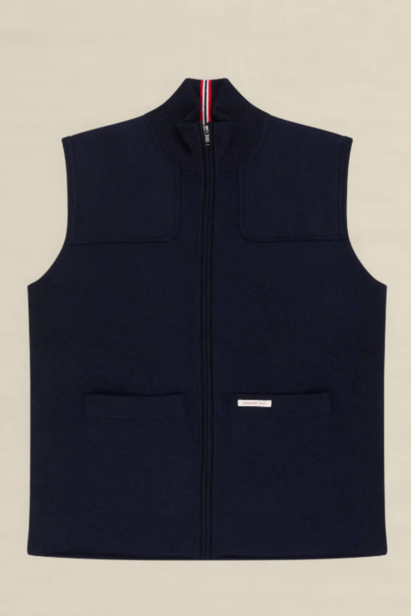 A navy blue zip-up fleece vest with a mock neck, two front patch pockets, and a small white brand label on the lower front pocket, shown flat against a light beige background.