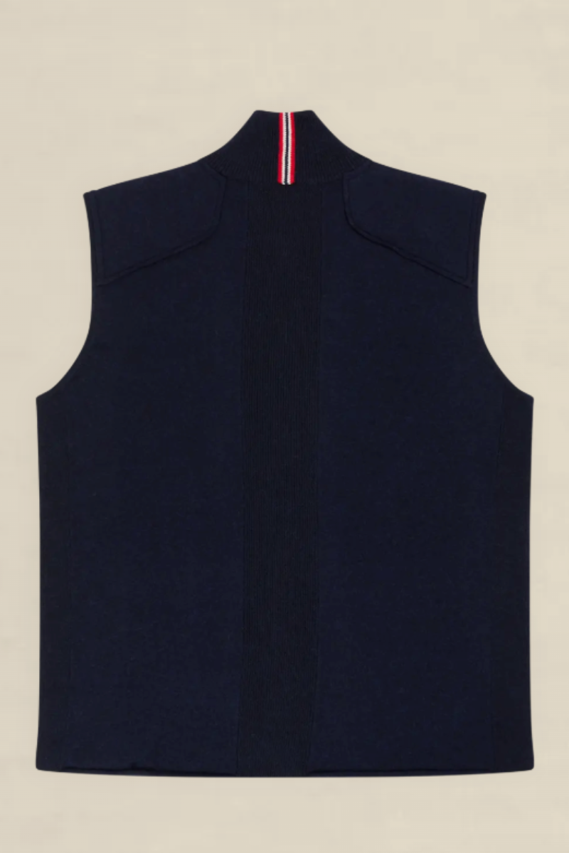 A sleeveless navy blue knit vest shown from the back, featuring a high mock neck with a vertical red, white, and blue striped accent at the collar, laid flat on a light beige background.